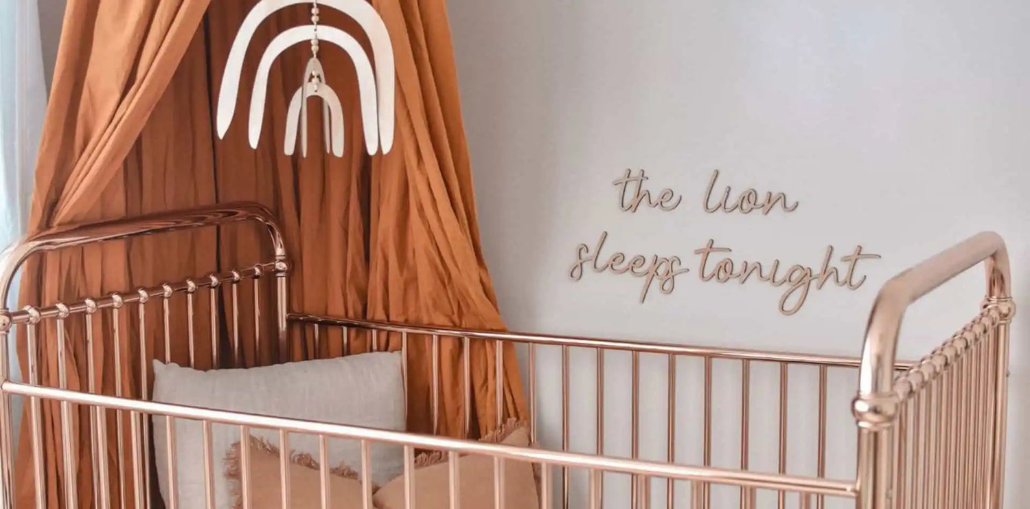 Metal crib with a terracotta-colored canopy and rainbow wall decor above it.